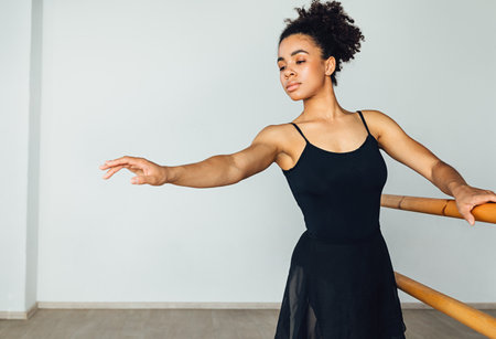 Young African American woman practicing ballet exercises holding a wooden handrailの写真素材