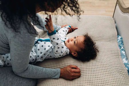 Cute baby boy playing with mother on a bedの写真素材