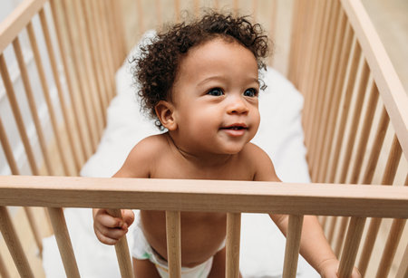Close up portrait of a toddler in a crib. Little boy standing in the bedroom.の写真素材