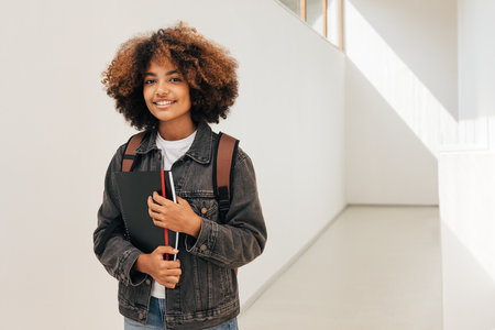 Young woman with curly hair standing in college corridor and looking at cameraの写真素材