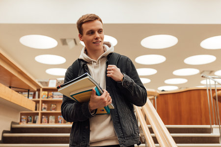 Teenager holding a books standing in college libraryの写真素材