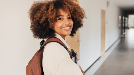 Smiling girl looking back while walking in high school corridorの写真素材