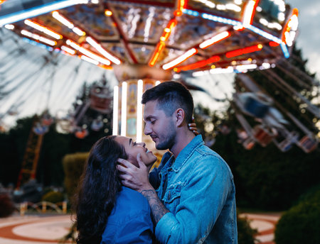 Happy couple in an amusement park. Young couple in love hugging and looking at each other against the carousel.の写真素材