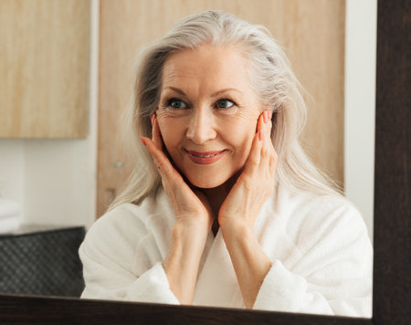 Portrait of a smiling mature woman with grey hair looking at a mirror in bathroomの写真素材