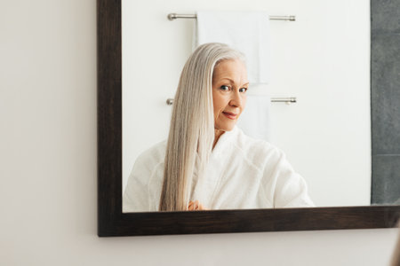 Portrait of an aged woman with long grey hair. Female looking in the mirror admires her hair.の写真素材
