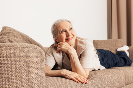 Dreaming senior woman on a sofa. Aged female looking away and smiling in the living room.の写真素材