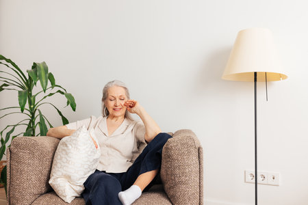 Aged smiling woman with grey hair relaxing in an armchair at homeの写真素材