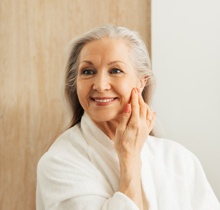 Smiling senior female touching her face with hand in front of a mirror