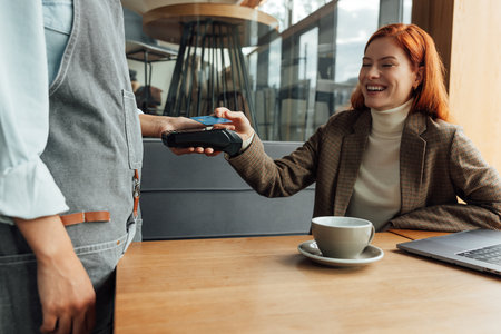 Happy woman paying for breakfast by card in coffee shopの写真素材