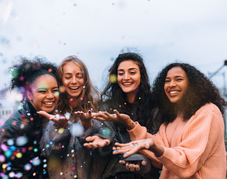 Four happy females throwing confetti outdoors in the eveningの写真素材