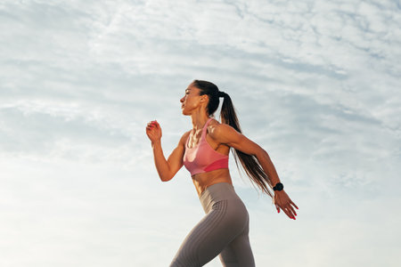 Sportswoman with long hair running outdoors against skies. Slim female jogger running on the...