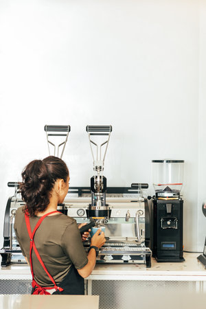 Back view of a female barista making coffee. Woman in apron working in a small coffee shop.の写真素材