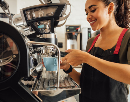 Smiling female barista using coffee maker in cafeteria. Woman in apron preparing espresso.の写真素材