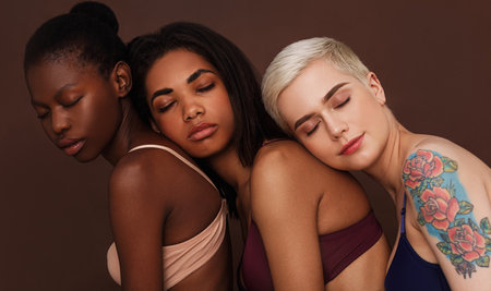 Portrait of three diverse women in lingerie standing together with eyes closed against a brown backgroundの写真素材