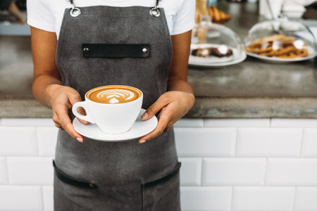 Unrecognizable waitress holding a cup of latte with rosetta in cafeの写真素材