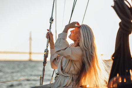 Side view of a mature woman sitting on a yacht and adjusting her hair at sunsetの写真素材