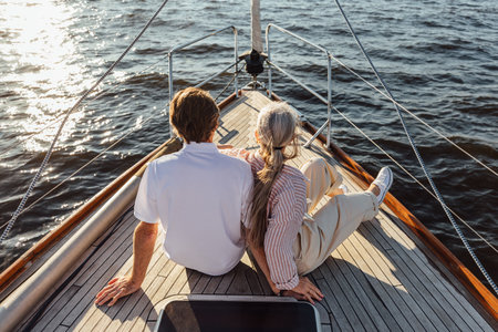 Rearview of two mature people sitting on a yacht bow. Loving senior couple enjoying a boat trip.の写真素材