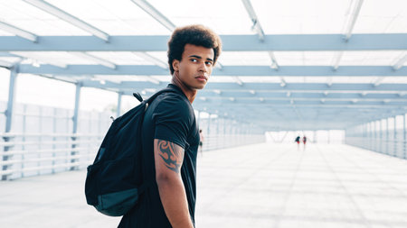 Male athlete with backpack looking back, walking in pedestrian bridgeの写真素材
