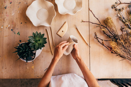 Shot from above hands of female ceramic artist molding a mug