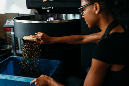 Female barista using industrial coffee roasting machine in cafeの写真素材