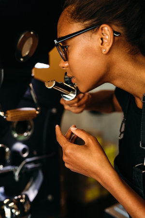 Side view of young barista smelling roasted coffee beans for aroma