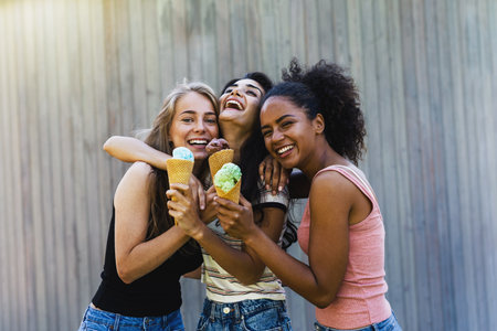 Three laughing girl friends with ice cream standing outdoors together