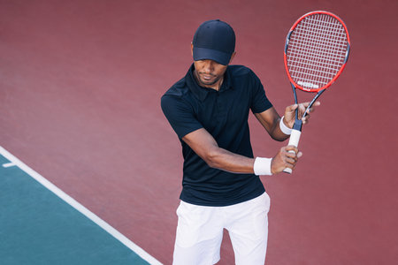 Professional tennis player in a cap holding a racket on a hard courtの写真素材