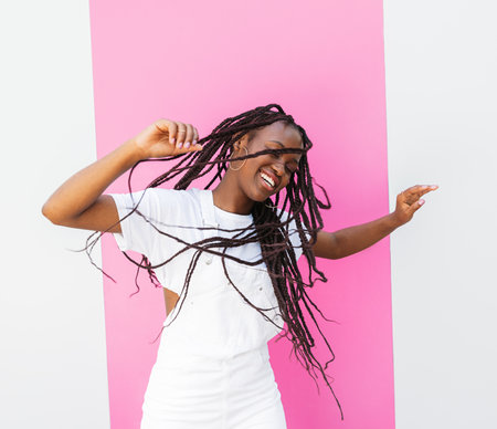 Happy girl in white overall dancing outdoors at a wall with pink stripeの写真素材