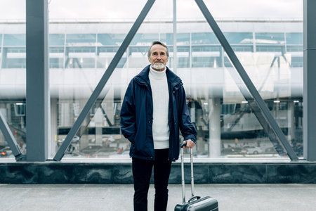 Handsome mature traveler standing with his suitcase in airport terminalの写真素材