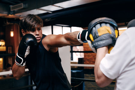 Young male boxer practicing punches in gym with coachの写真素材