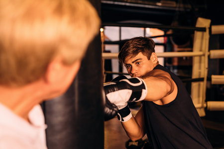 Young boxer hitting a punching bag while coach holding