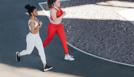 Shot from above of two females running together outdoors. High angle of two female friends jogging...