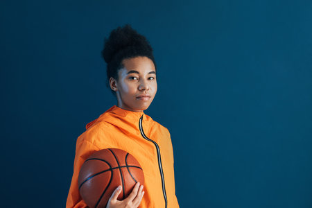 Young confident female with a basketball looking at camera. Woman wearing orange fitness attire holding a basketball.の写真素材