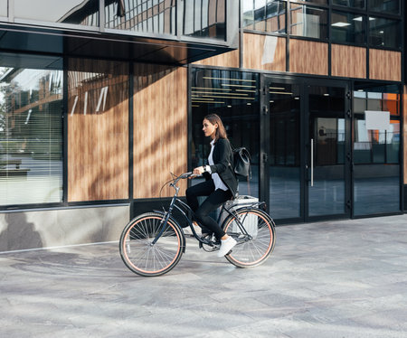 Woman in formal wear riding a bicycle against a business building. Businesswoman is going to work on a bicycle.の写真素材