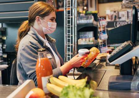Female cashier in mask using barcode scanner at checkoutの写真素材