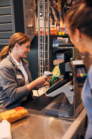 Smiling cashier using a barcode scanner on a salad pack while customer waitingの写真素材