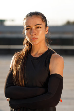 Portrait of a young sportswoman with arms crossed. Highly detailed portrait of a female runner wearing arm sleeves looking at camera.の写真素材