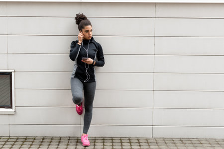 Young female jogger with earphones and smartphone listening to music