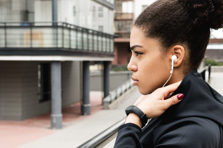 Sporty woman with hooded jacket standing in urban environment, looking away