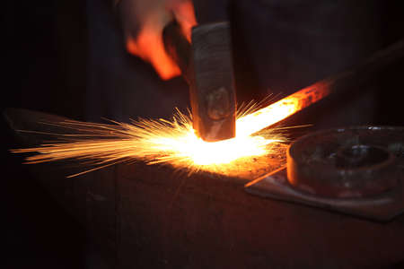 Hands of smith with hammet and steel stick on the anvil