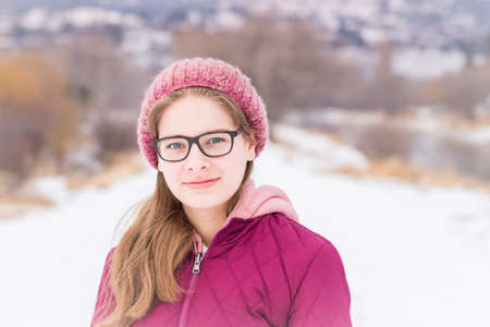 Portrait of teenage girl in pink hat and coat standing in winter landscape and smiling at cameraの写真素材