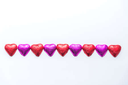 Row of alternating pink and red foil wrapped chocolate hearts on white backgroundの写真素材