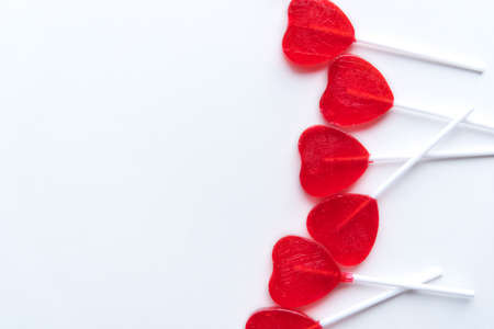 Red heart shaped Valentine lollipops scattered across right side of white background