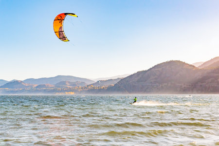PENTICTON, BRITISH COLUMBIA, CANADA - OCTOBER 24, 2017 a kiteboarder races across Skaha Lake as the sun sets behind the mountains. The lake is a popular kiteboarding location in the Okanagan Valley.のeditorial素材
