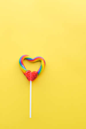 Cute heart-shaped rainbow swirl lollipop on solid yellow background portrait formatの写真素材