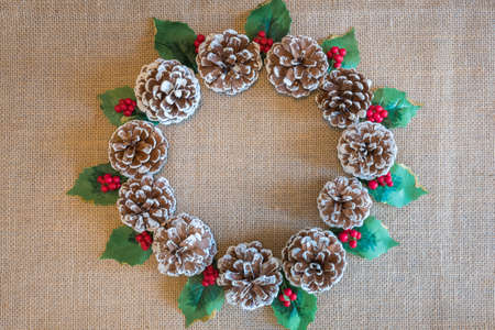 Christmas wreath of pinecones, holly leaves, and red berries on rustic fabric background