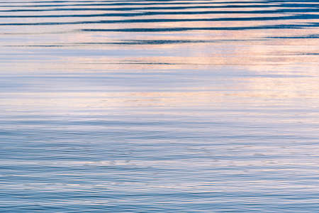 Gentle ripples on surface of lake reflecting pink, purple, and blue colors in sky at sunsetの写真素材