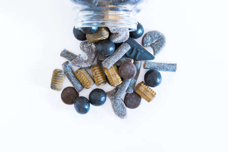 Jar of assorted salmiakki spilling onto solid white background flat -lay