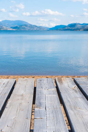 Weathered gray picnic table in foreground with view of lake and mountains in backgroundの写真素材