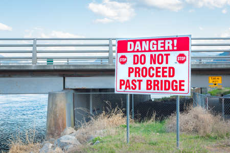 Large danger sign where river channel enters lake under bridgeの写真素材